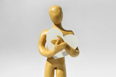 Photo of Yellow plasticine human figure with paper heart on white background
