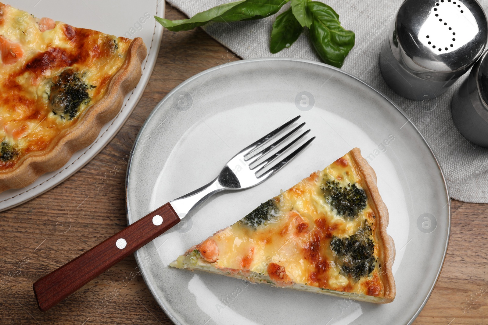 Photo of Piece of delicious homemade salmon quiche with broccoli and fork on wooden table, flat lay