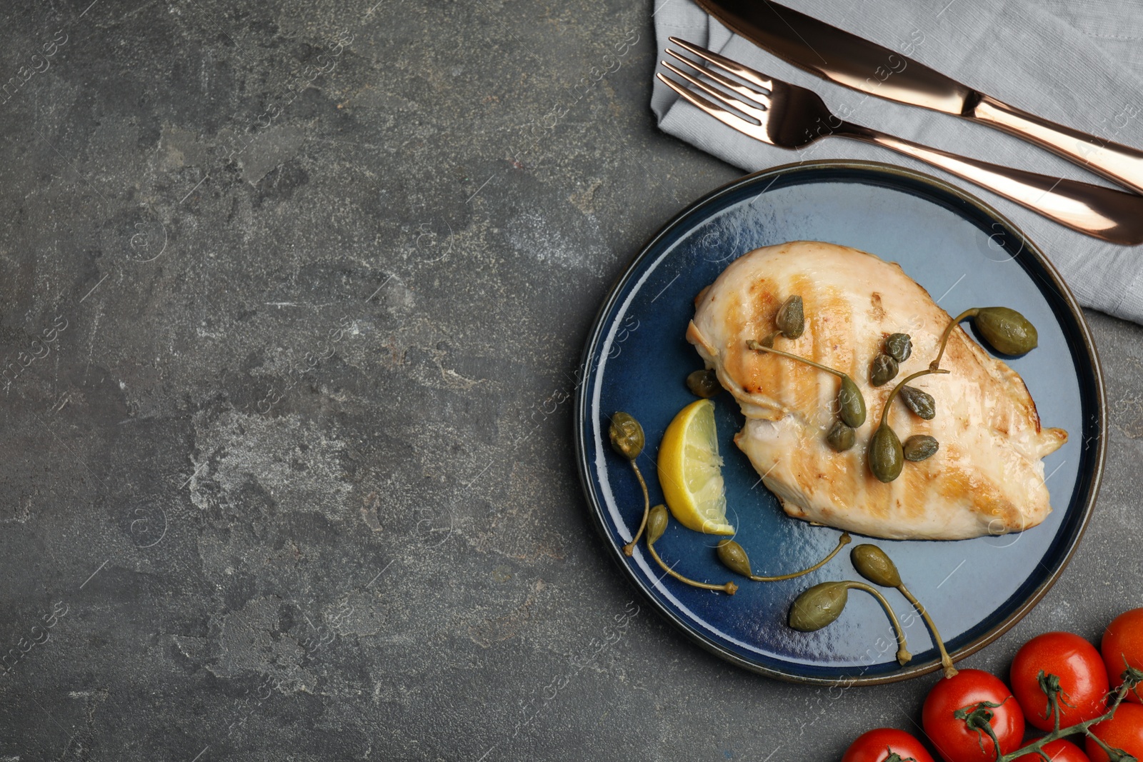 Photo of Delicious cooked chicken fillet with capers and lemon slice served on grey table, flat lay. Space for text