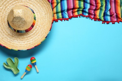 Mexican sombrero hat, maracas, toy cactus and colorful poncho on light blue background, flat lay. Space for text
