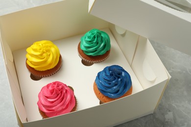 Photo of Box with different cupcakes on grey table, closeup