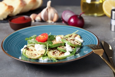 Photo of Delicious grilled zucchini slices served with cottage cheese and tomatoes on grey table, closeup