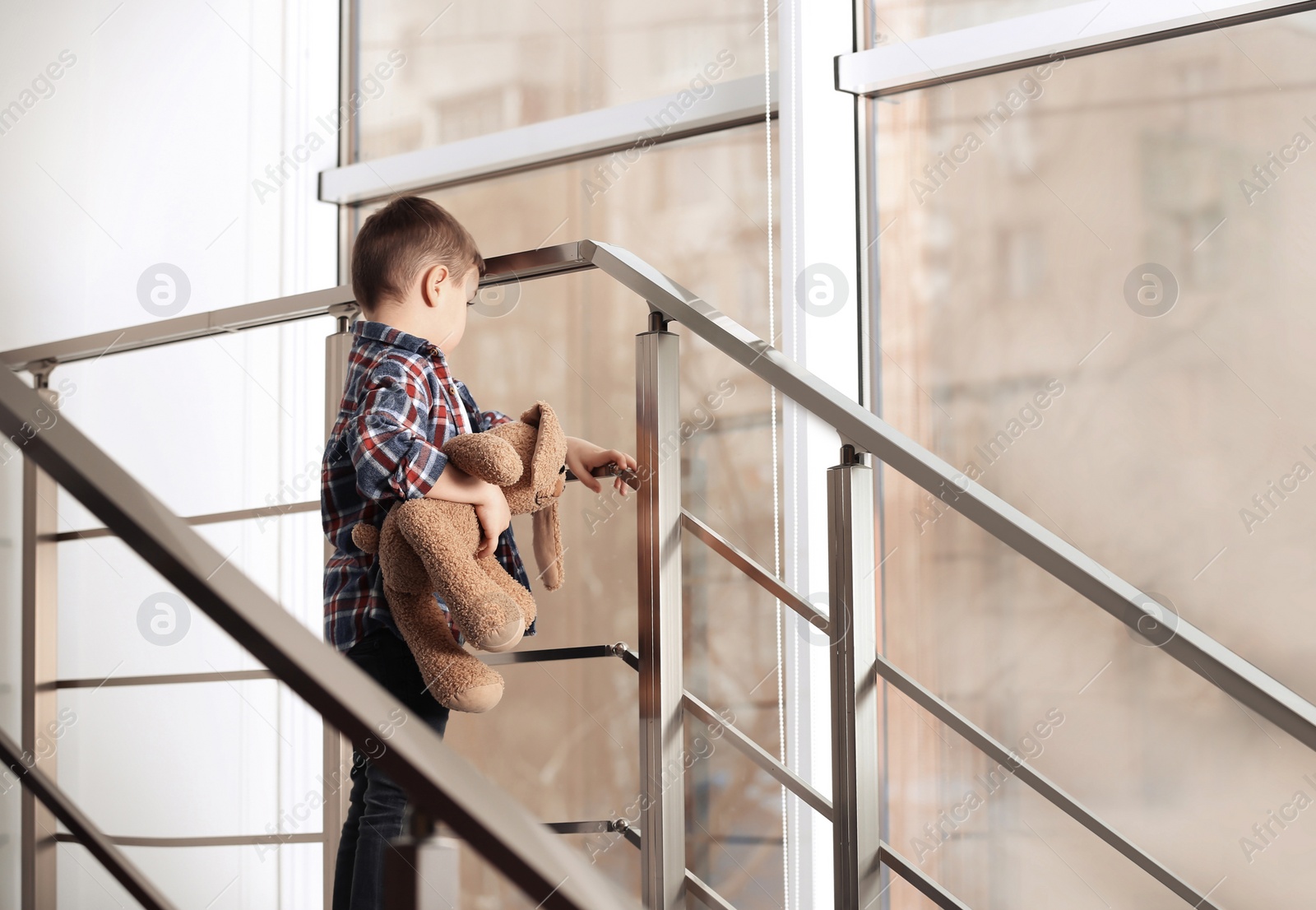 Photo of Sad little boy with toy on stairs indoors