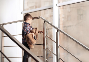 Sad little boy with toy on stairs indoors
