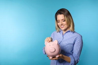 Beautiful woman putting money into piggy bank on color background. Space for text