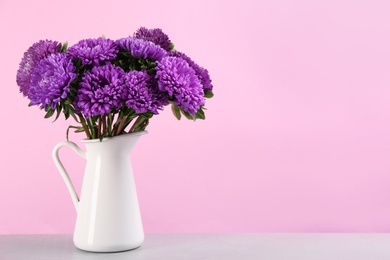 Photo of Beautiful asters in jug on table against pink background, space for text. Autumn flowers