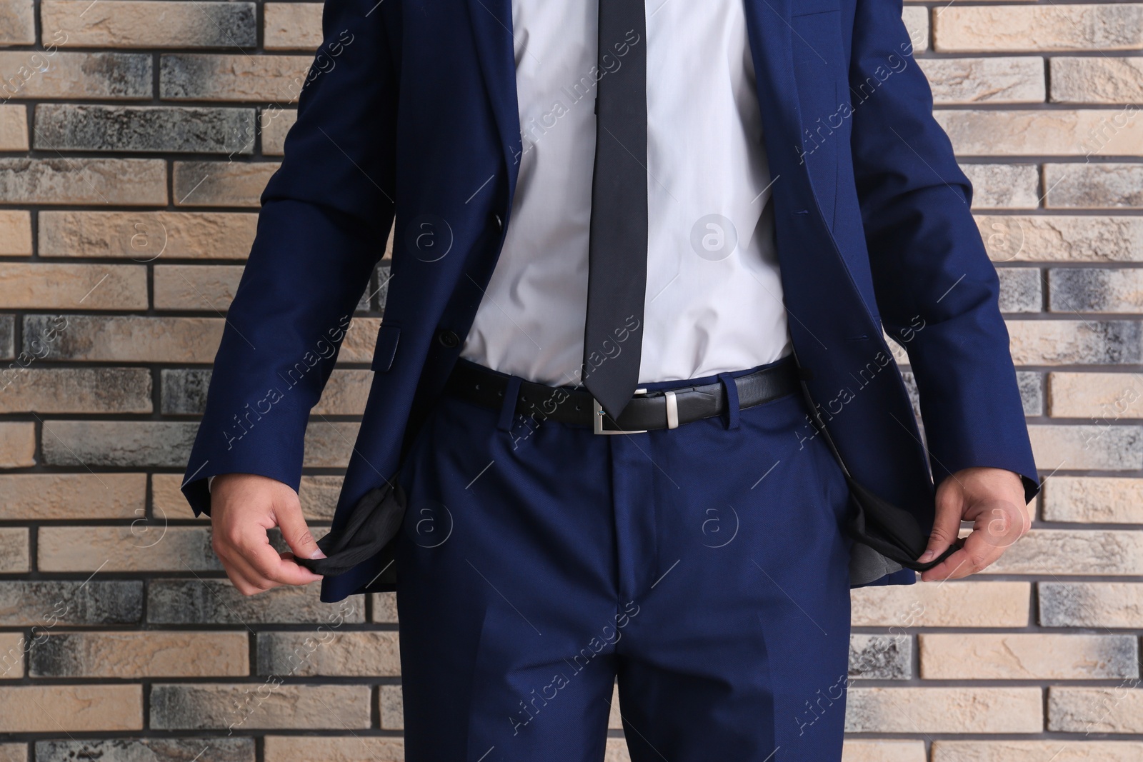 Photo of Businessman showing empty pockets near brick wall, closeup