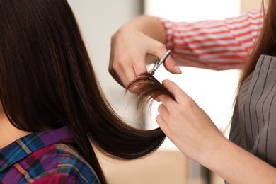 Barber making stylish haircut with professional scissors in beauty salon, closeup