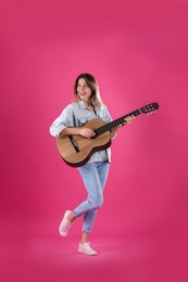 Young woman playing acoustic guitar on color background