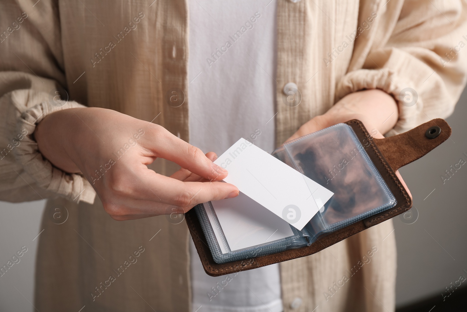 Photo of Woman holding leather business card holder and blank card on grey background, closeup