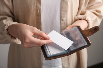 Woman holding leather business card holder and blank card on grey background, closeup