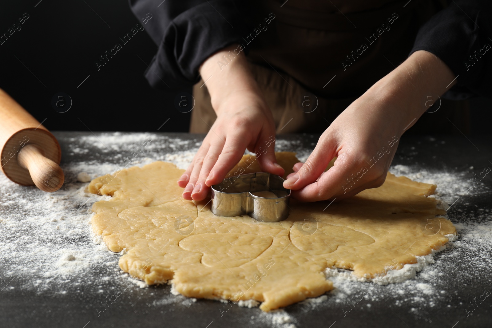 Photo of Shortcrust pastry. Woman making cookies with cutter at grey table, closeup