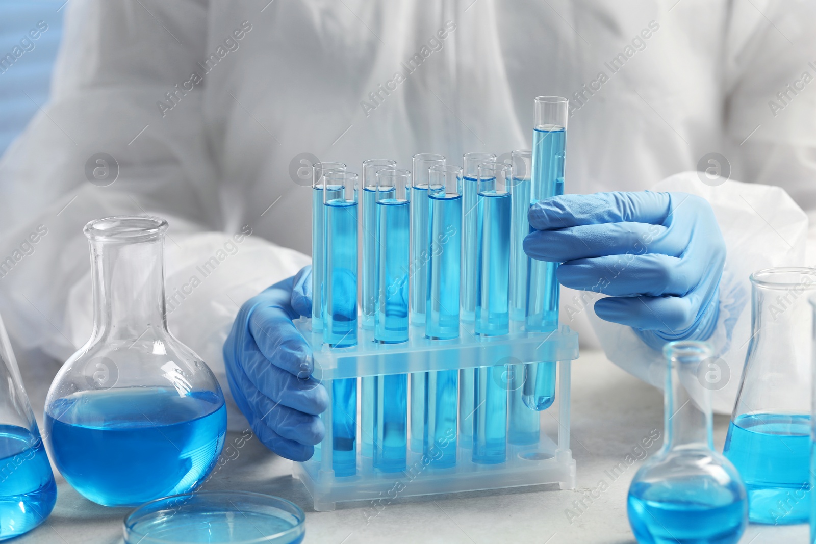 Photo of Scientist taking test tube with light blue liquid at white table in laboratory, closeup