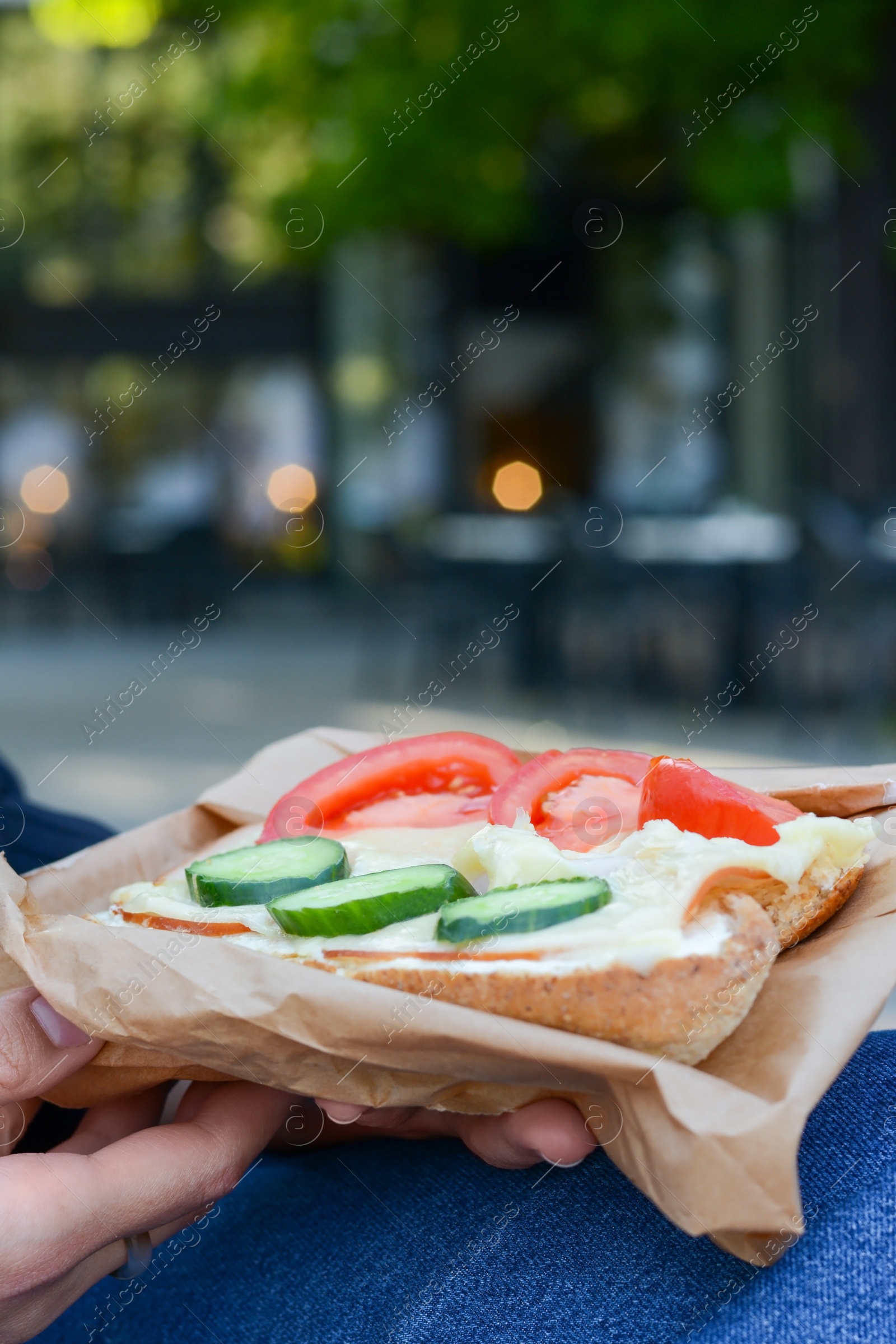 Photo of Woman holding tasty sandwich with vegetables outdoors, closeup. Street food