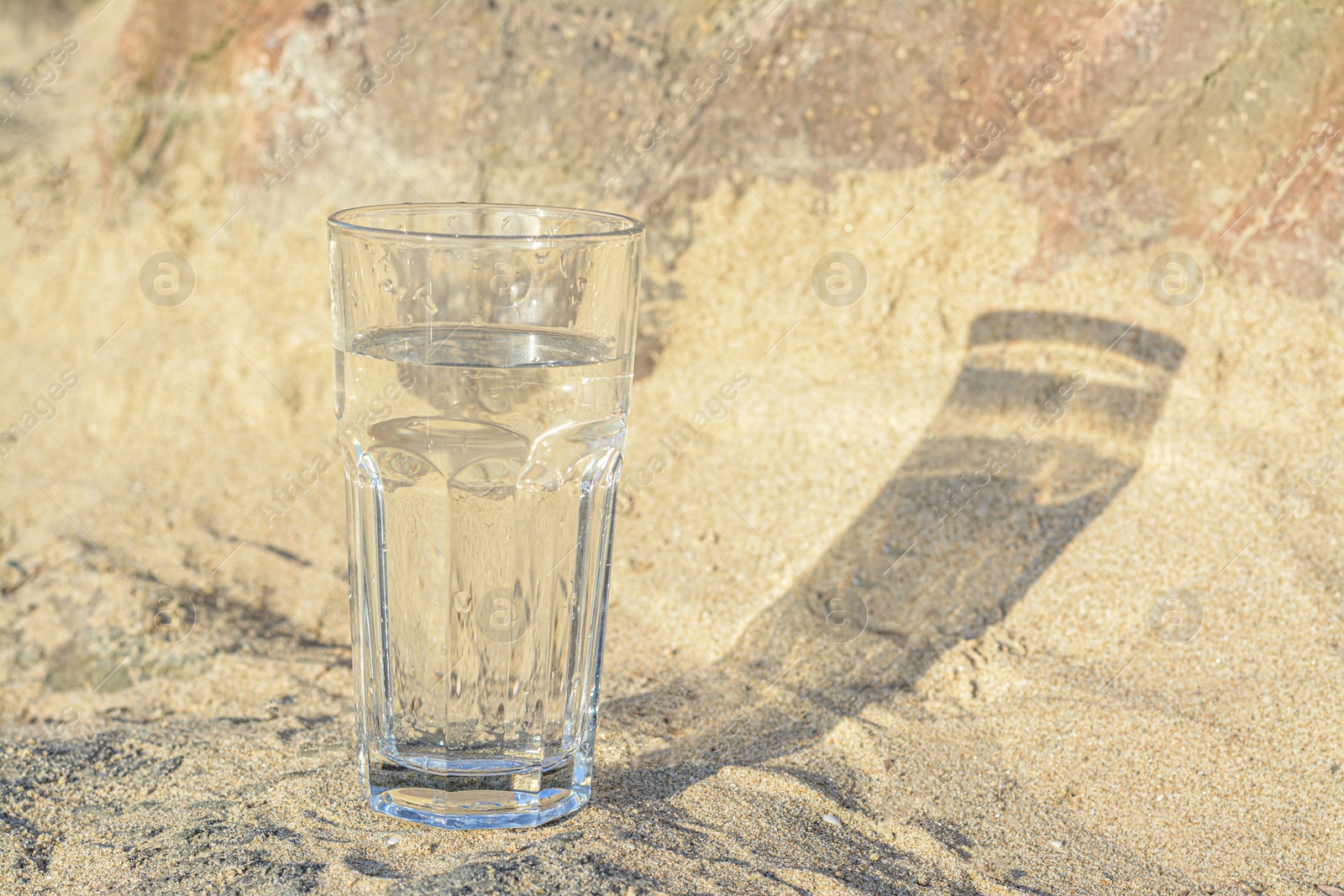 Photo of Glass of clean water on sand outdoors. Space for text