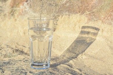 Glass of clean water on sand outdoors. Space for text