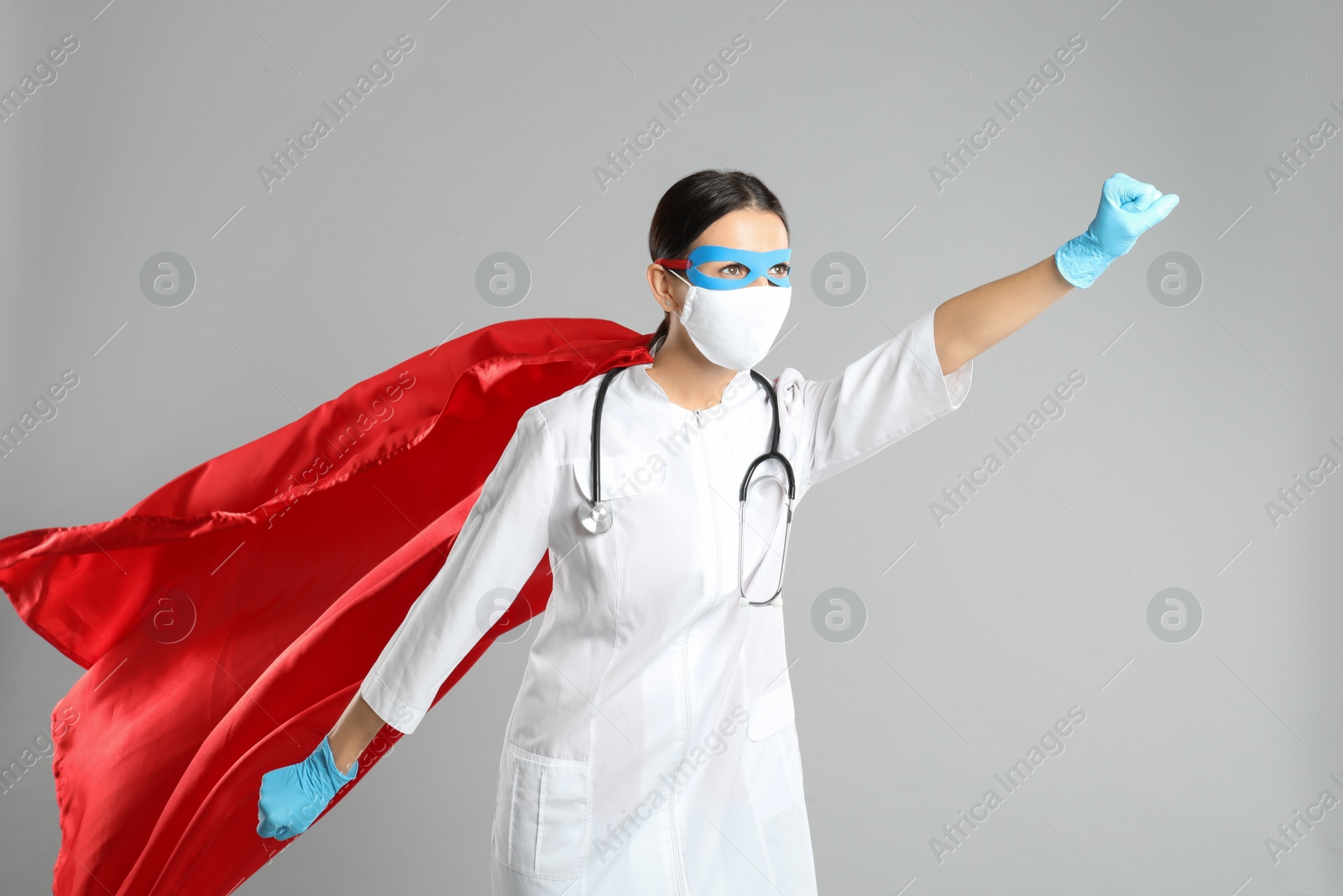 Photo of Doctor dressed as superhero posing on light grey background. Concept of medical workers fighting with COVID-19