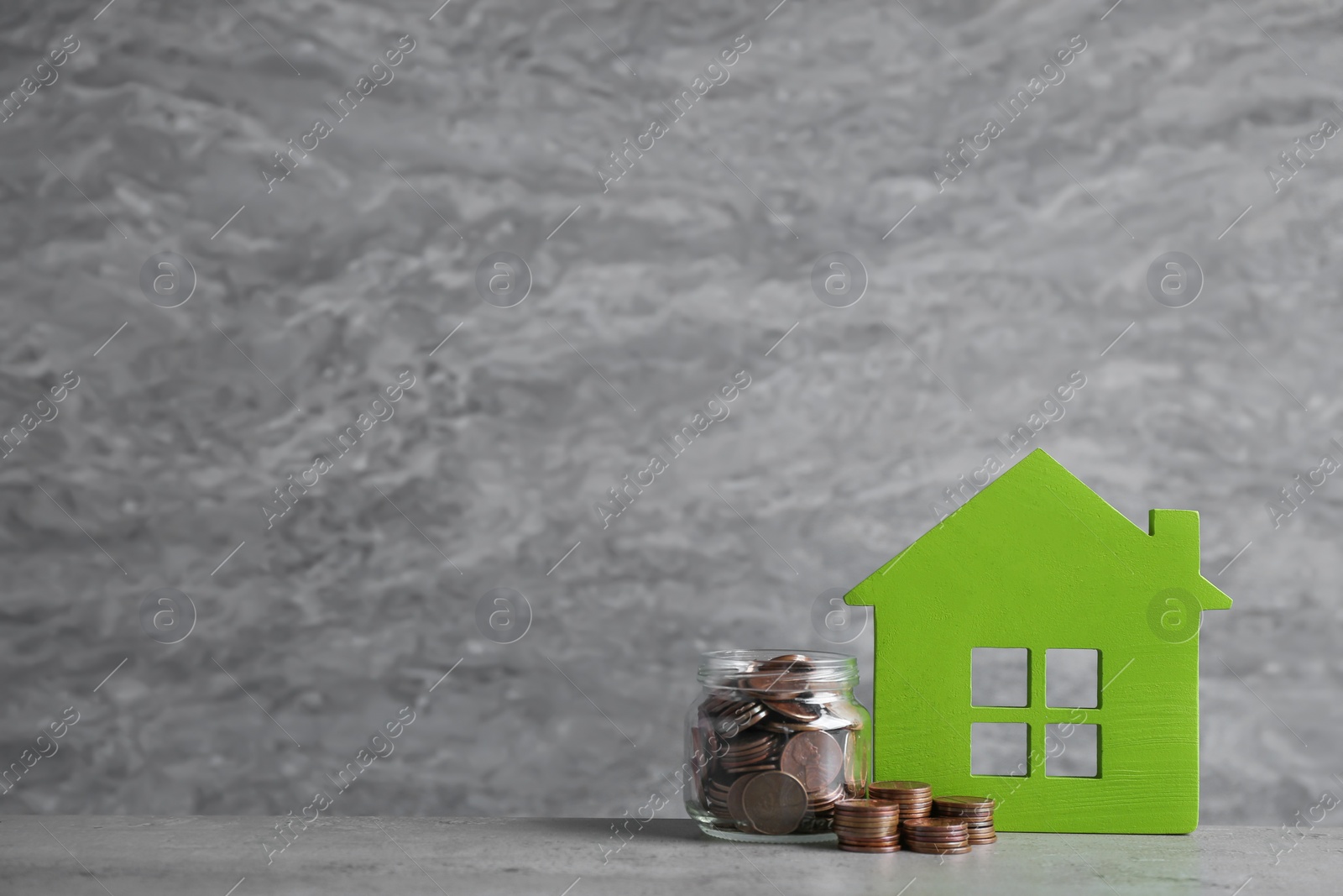 Photo of House model and jar with coins on table against grey background. Space for text