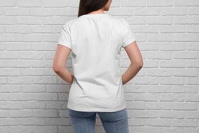 Woman wearing stylish T-shirt near white brick wall, closeup