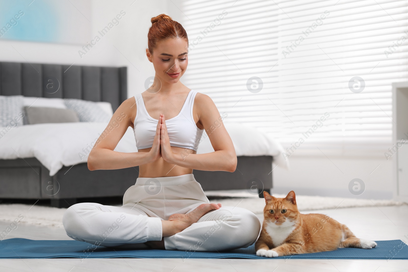 Photo of Beautiful woman with cute red cat practicing yoga on mat at home