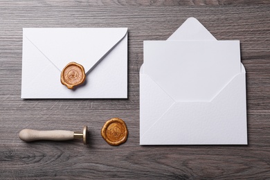 Envelopes with wax seal and stamp on wooden table, flat lay