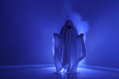 Photo of Creepy ghost. Woman covered with sheet in blue light, space for text