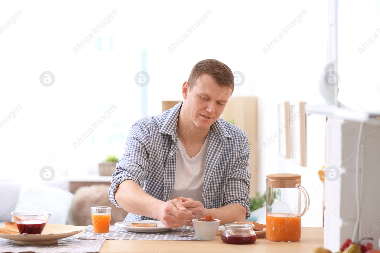 Photo of Young man spreading jam onto tasty toasted bread at table