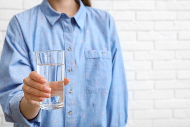 Photo of Woman holding glass of water near brick wall, closeup with space for text. Refreshing drink