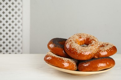 Many delicious fresh bagels on white wooden table, space for text