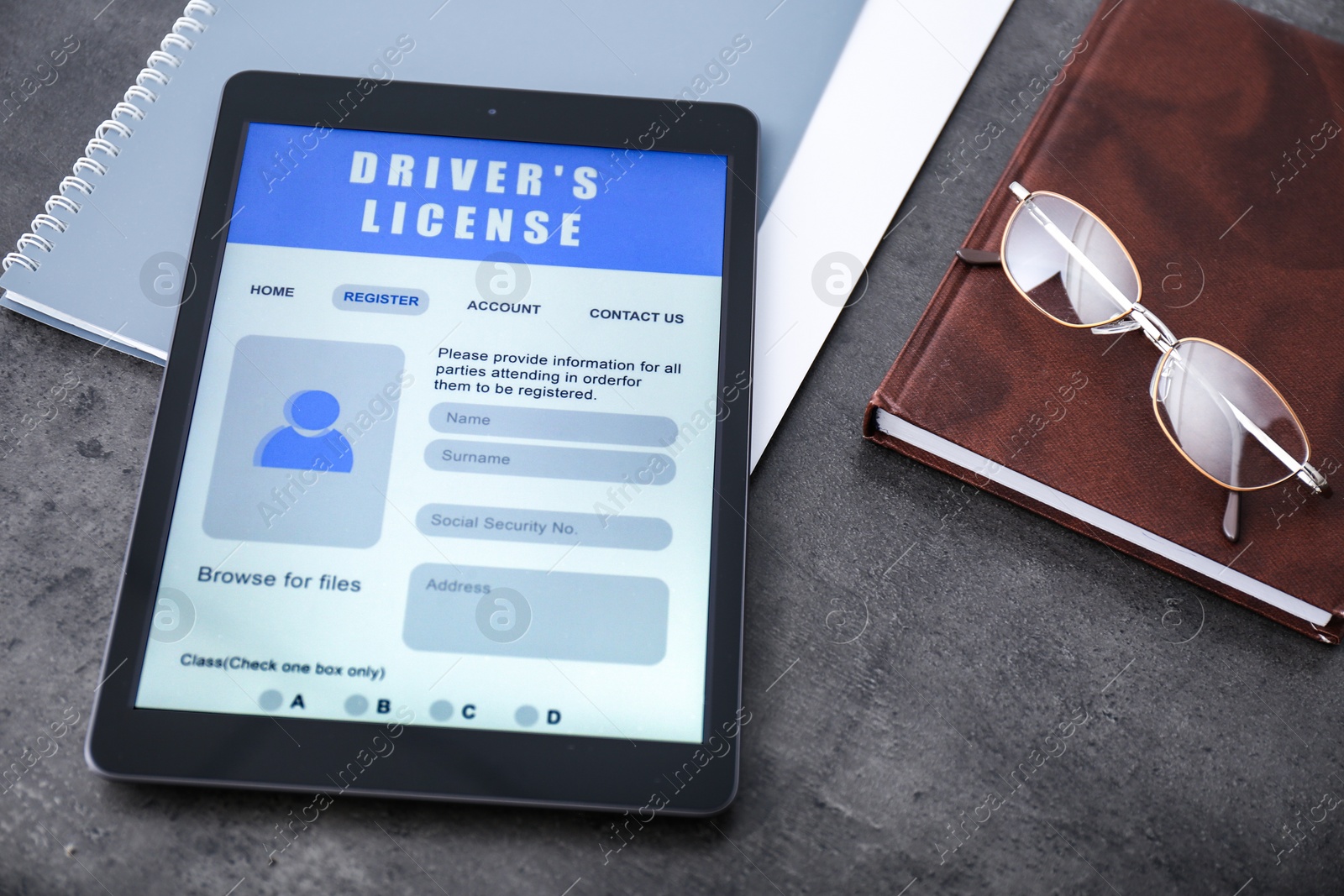 Photo of Tablet with driver's license application form, glasses and stationery on grey table
