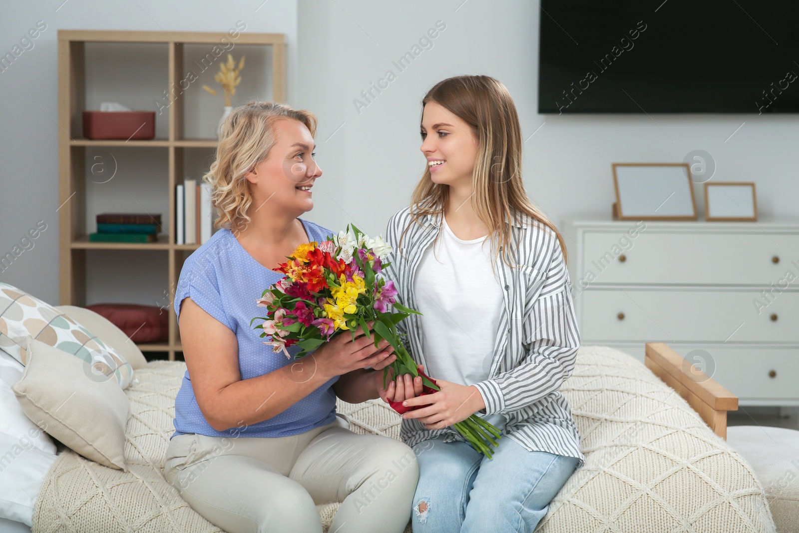 Photo of Young daughter congratulating her mom with flowers at home. Happy Mother's Day