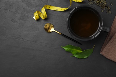 Photo of Cup of herbal diet tea and measuring tape on black table, flat lay with space for text. Weight loss concept