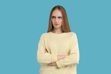 Photo of Resentful woman with crossed arms on light blue background