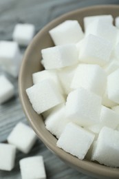 Photo of White sugar cubes in bowl on wooden table, closeup