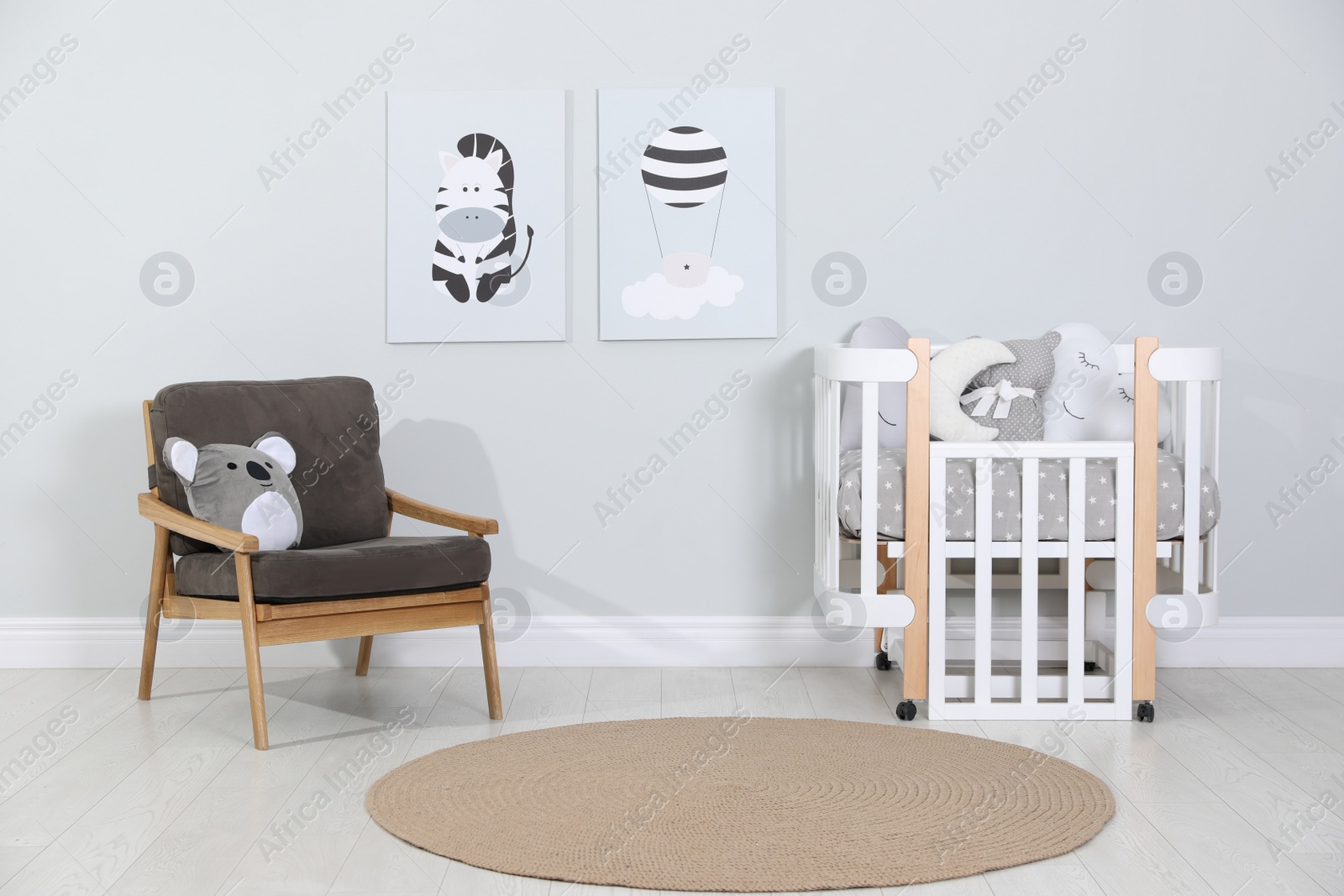 Photo of Crib and armchair near wall with pictures in cozy baby room. Interior design