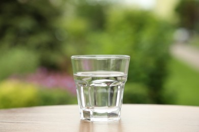 Glass of fresh water on wooden table outdoors