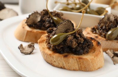 Photo of Delicious bruschettas with truffle sauce and caperberries on white plate, closeup