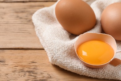 Photo of Whole and cracked eggs on wooden table, closeup. Space for text