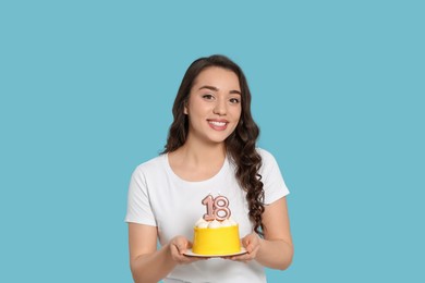 Coming of age party - 18th birthday. Woman holding delicious cake with number shaped candles on light blue background