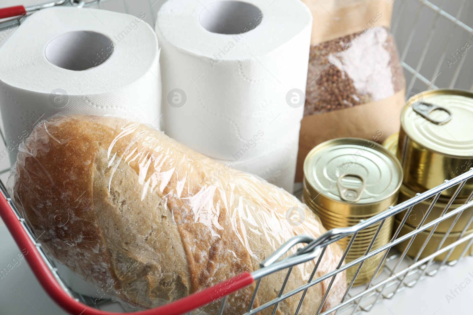 Photo of Shopping basket with products and toilet paper rolls on table, closeup. Panic caused by virus