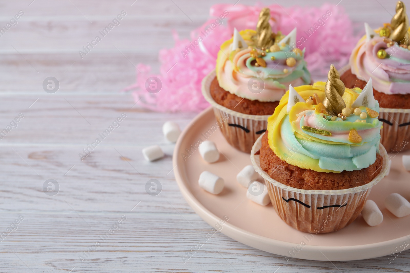 Photo of Cute sweet unicorn cupcakes on white wooden table, space for text