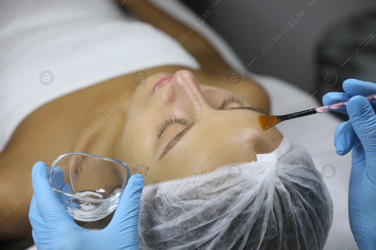 Photo of Cosmetologist applying cosmetic product for chemical peeling on client's face in salon