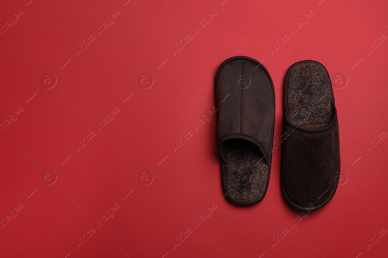 Photo of Pair of brown slippers on red background, top view. Space for text