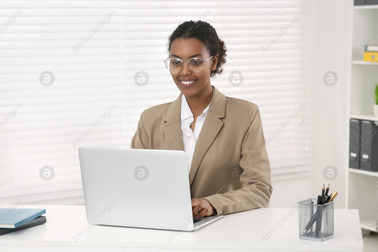 Photo of Smiling African American intern working on laptop at white table in office