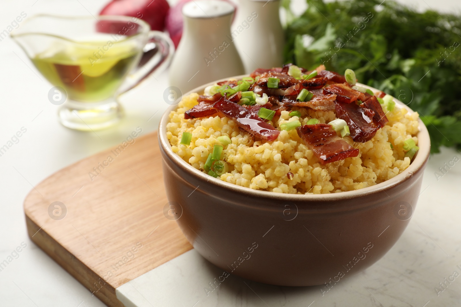 Photo of Tasty millet porridge with bacon and green onion in bowl on table, closeup