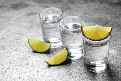 Photo of Mexican Tequila shots with salt and lime slices on grey table