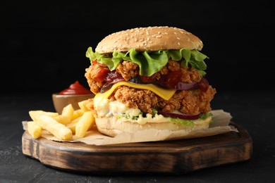 Photo of Delicious burger with crispy chicken patty, french fries and sauce on black table, closeup