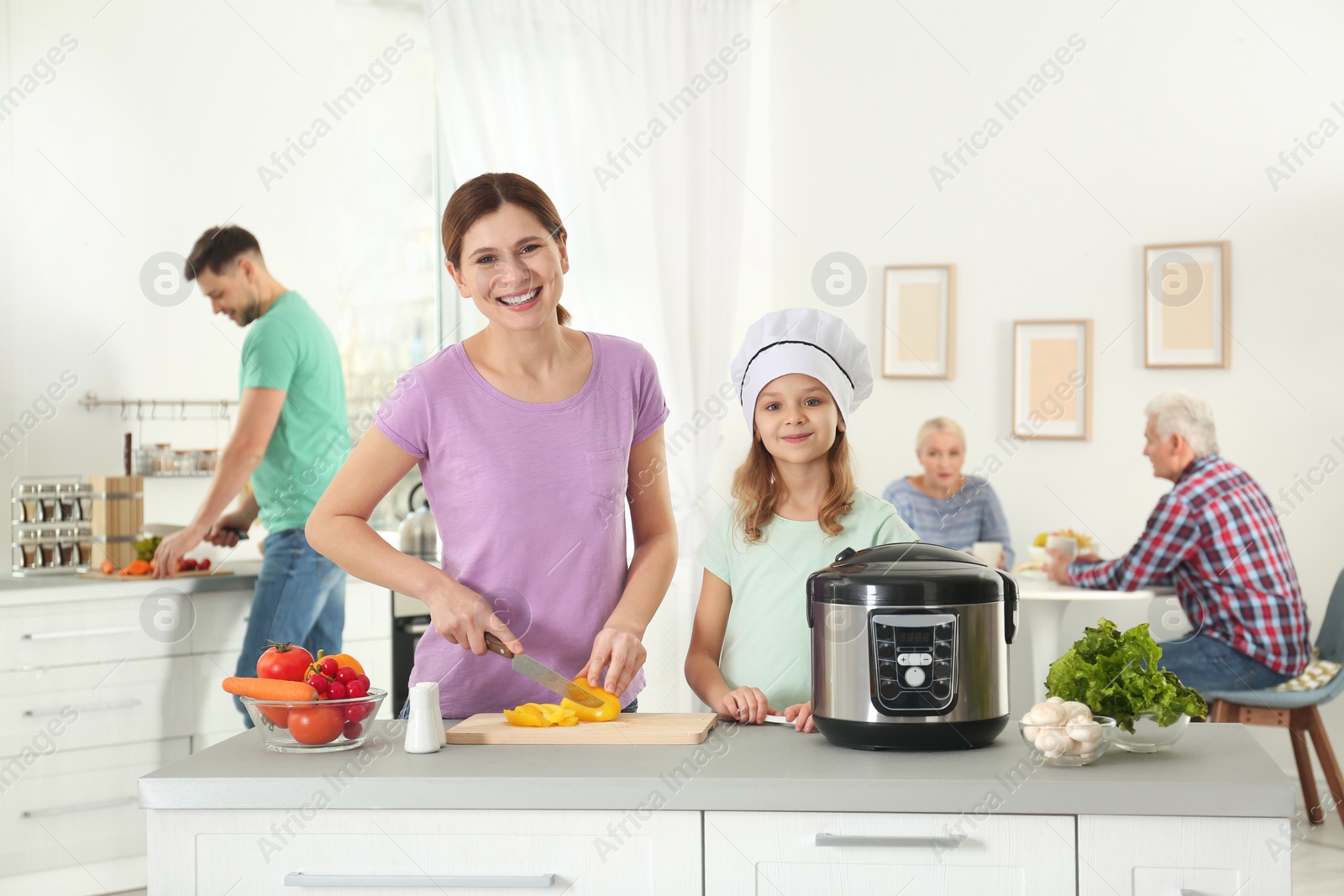 Photo of Mother and daughter preparing food with modern multi cooker in kitchen
