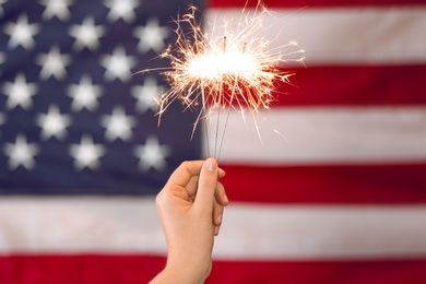 Woman holding bright burning sparklers against American flag, closeup