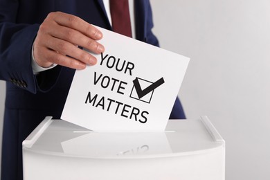 Man putting paper with text Your Vote Matters and tick into ballot box on light grey background